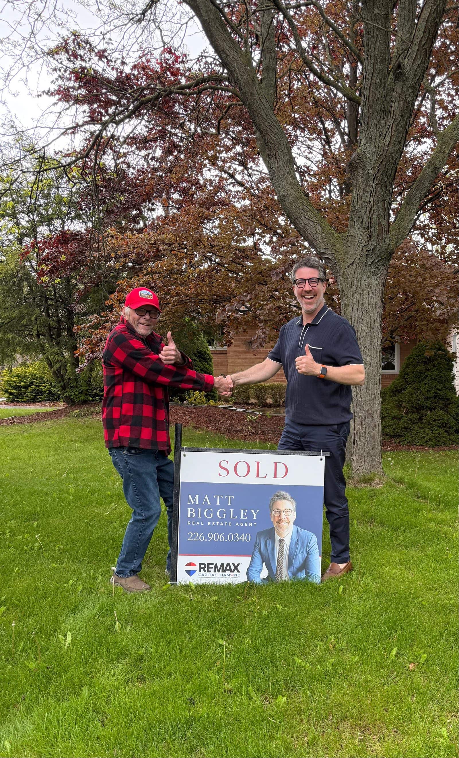 Matt Biggley shaking hands with a client beside a Sold sign on their front lawn
