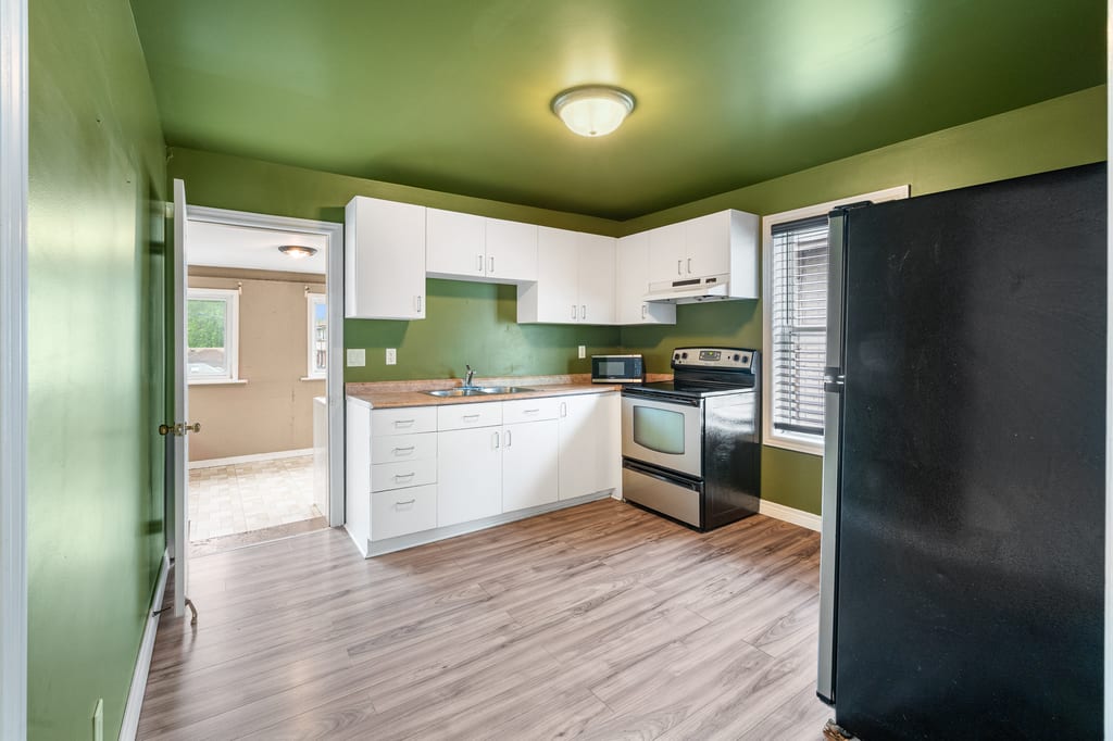Vacant upper-unit kitchen with green walls and white cabinetry