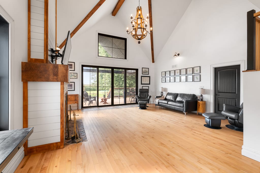 Great room with a 25 foot vaulted ceiling, exposed dark trusses, gas fireplace, and patio doors to the covered deck