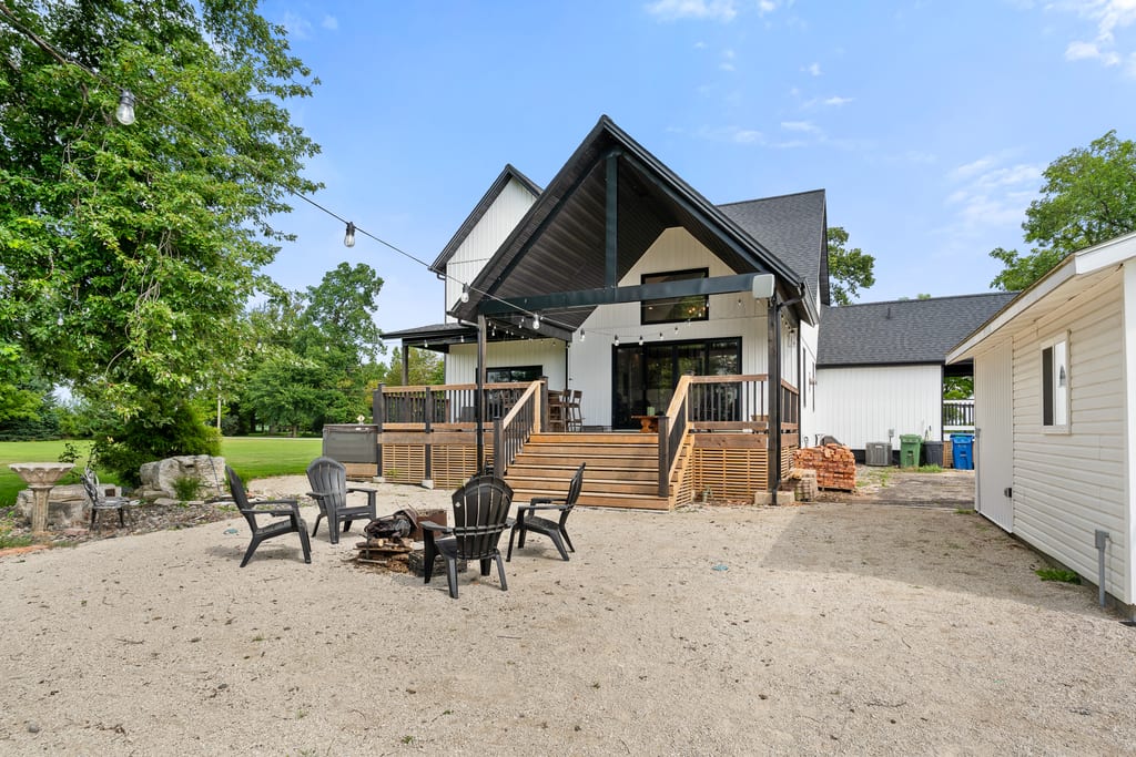 Rear elevation of the farmhouse with a raised deck, string lights, and a fire pit seating area