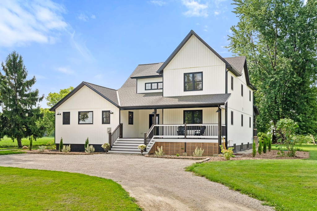 Angled view of the farmhouse front elevation, landscaping, and the gravel circular drive