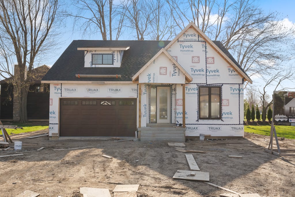 Front of the house at 252 Ford Road under construction in house wrap, with a dormer, a gabled entry porch, and a brown double garage door