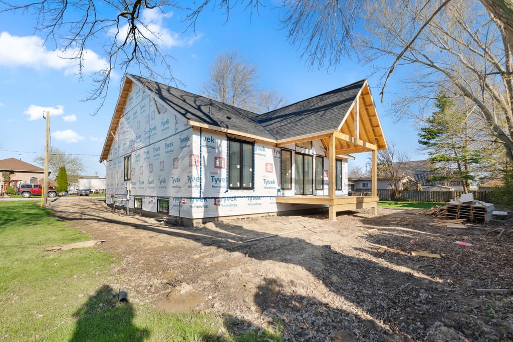 Rear corner of the house under construction, with tall black-framed windows and a timber-framed covered back porch