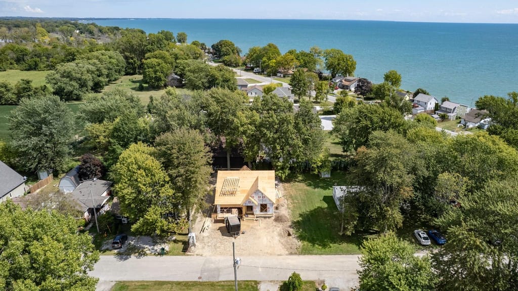 Aerial view of the house during framing among mature trees, with Lake Erie beyond the neighbouring homes