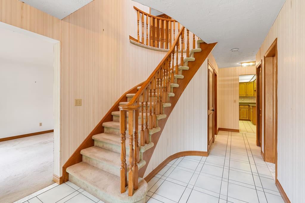 Curved staircase with a wood handrail rising from the tiled front hall