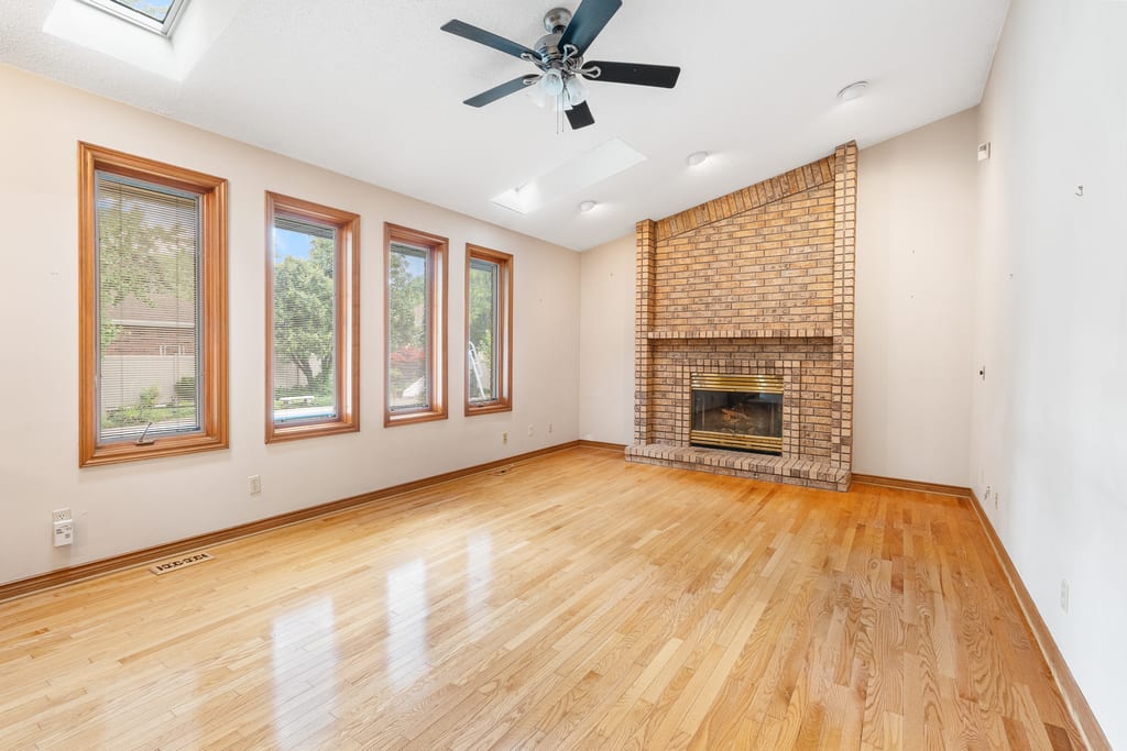 Vaulted living room with hardwood floors, a wall of windows, and a floor-to-ceiling brick fireplace