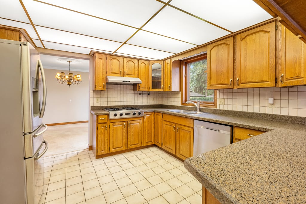 Kitchen with oak cabinetry, granite counters, tile floor, and a window over the sink
