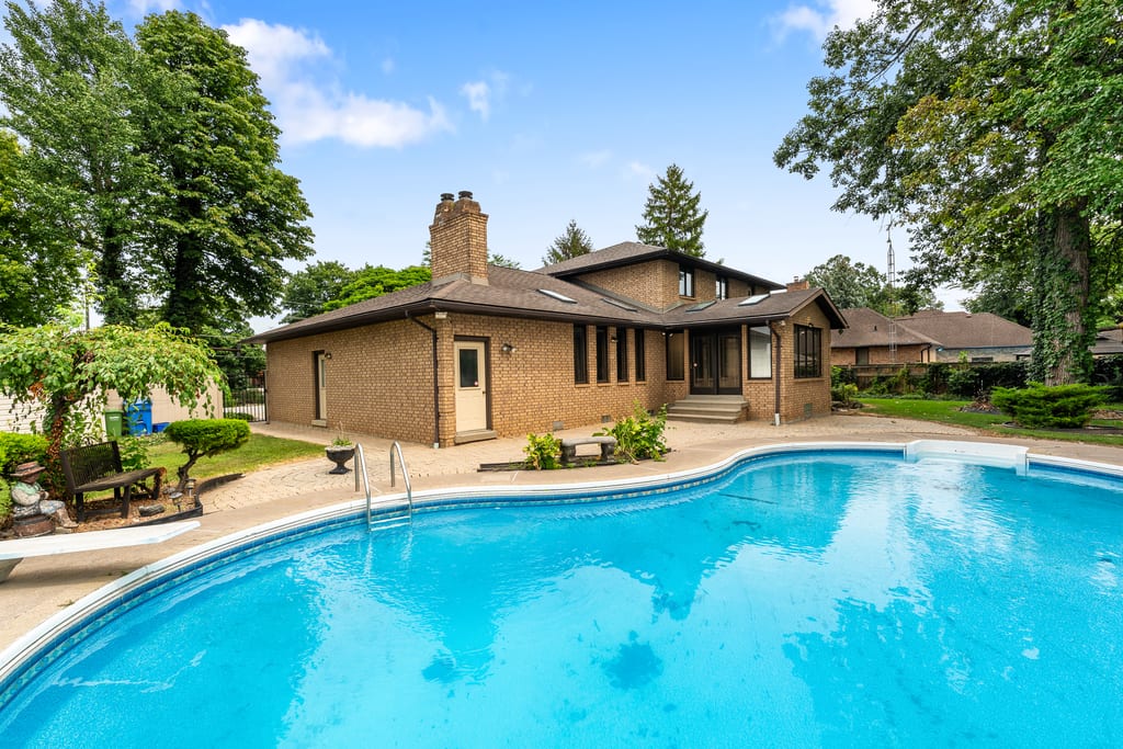 In-ground pool with paved surround, with the rear of the house behind it