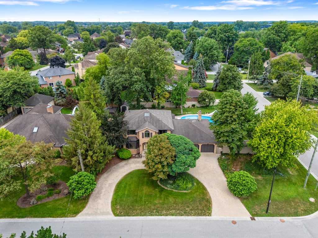 Aerial view of the property among mature trees, with the pool and circular drive visible