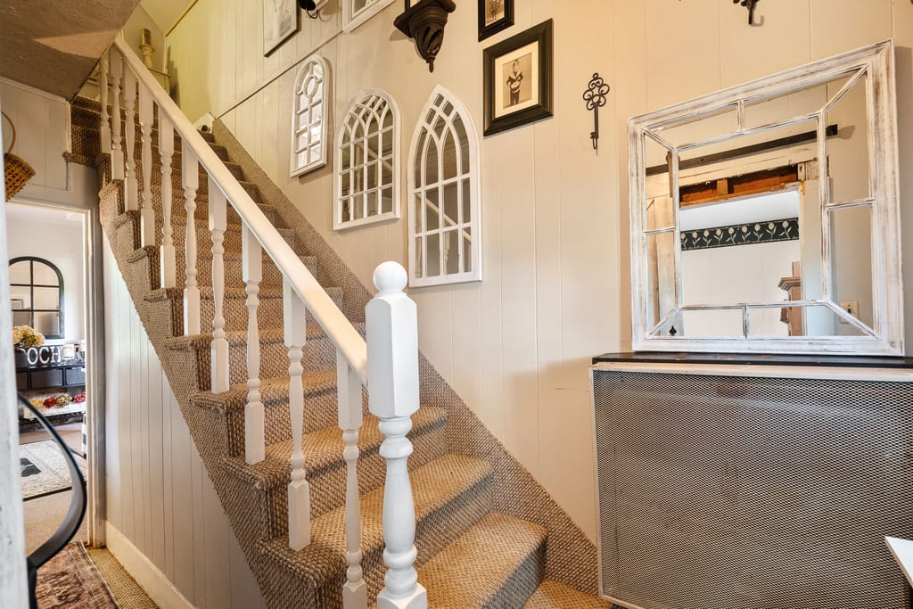 Narrow painted staircase with a wood handrail and framed pictures on the wall