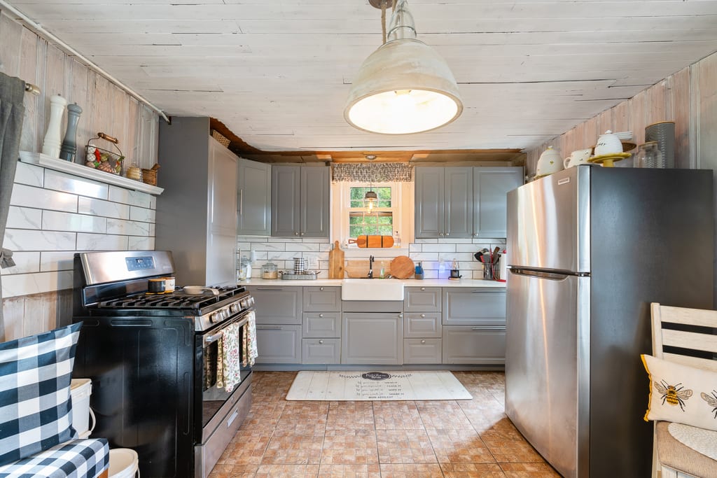 Kitchen with grey cabinetry, quartz counters, farmhouse sink, and tiled backsplash