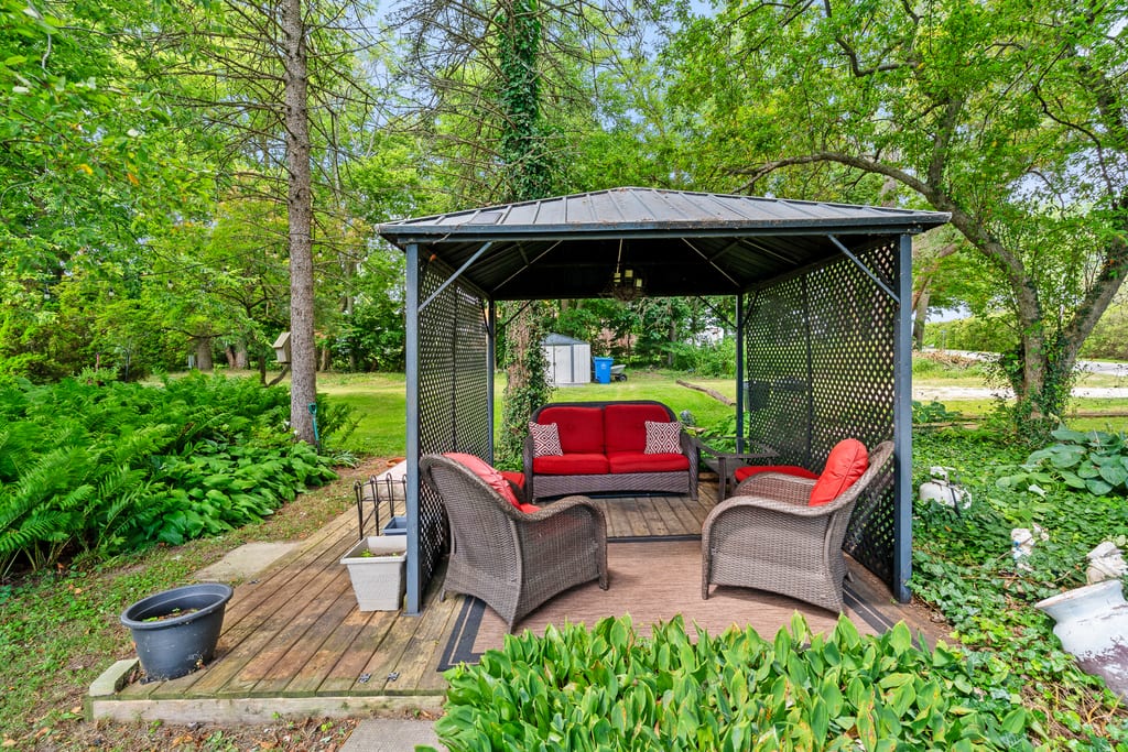 Covered gazebo with seating on a deck, surrounded by planting