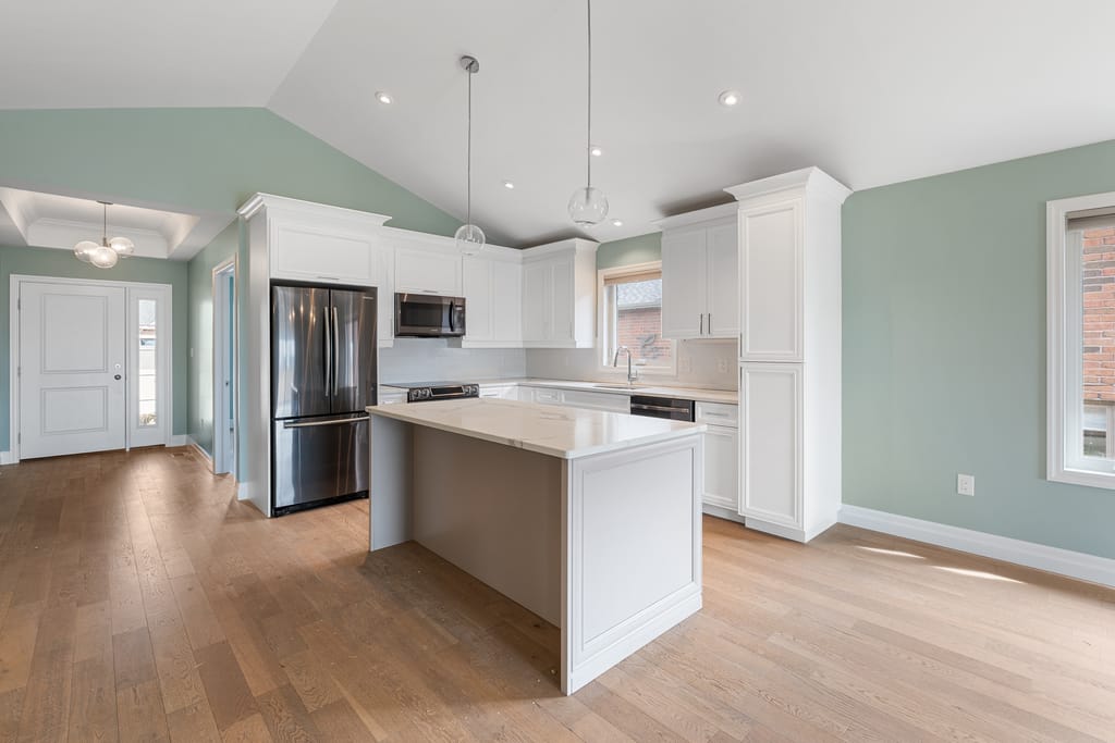 Kitchen with white cabinetry, a quartz-topped island, stainless appliances, and pendant lights under a cathedral ceiling