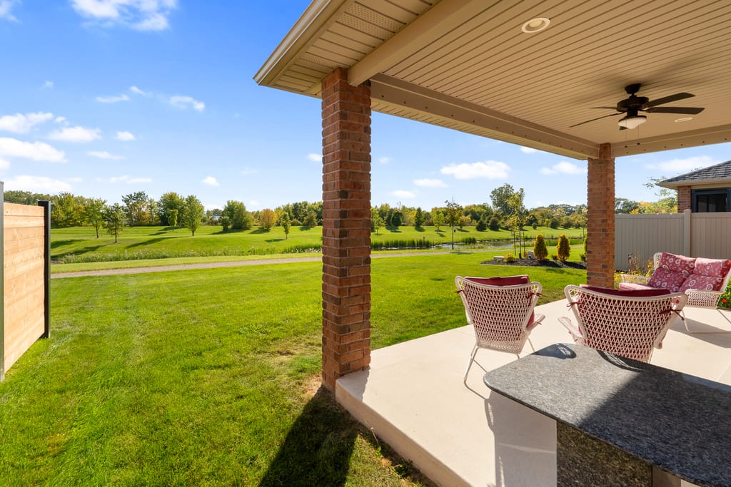 Covered back porch with a ceiling fan and seating, looking across the lawn to the walking trail and pond
