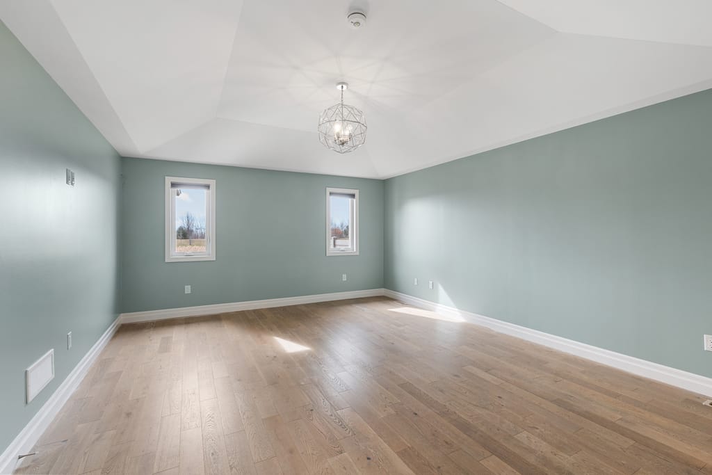 Primary bedroom with hardwood floors, a pendant light, and two windows