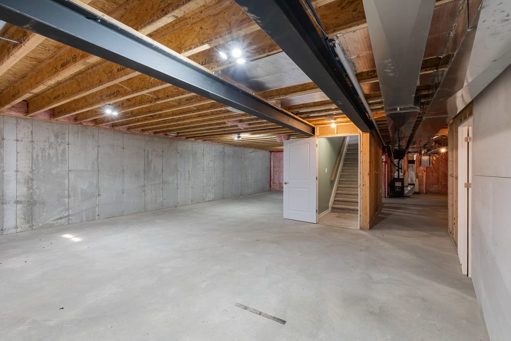Unfinished lower level with a concrete floor, a steel beam, and open ceiling joists