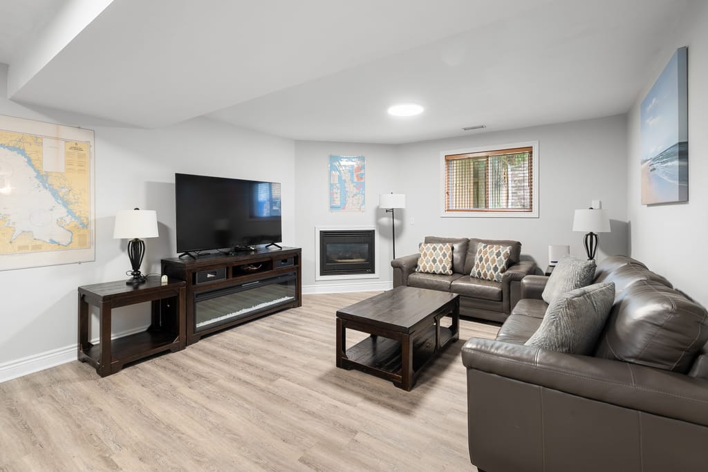 Finished lower level family room with a gas fireplace, light LVP flooring, and leather seating
