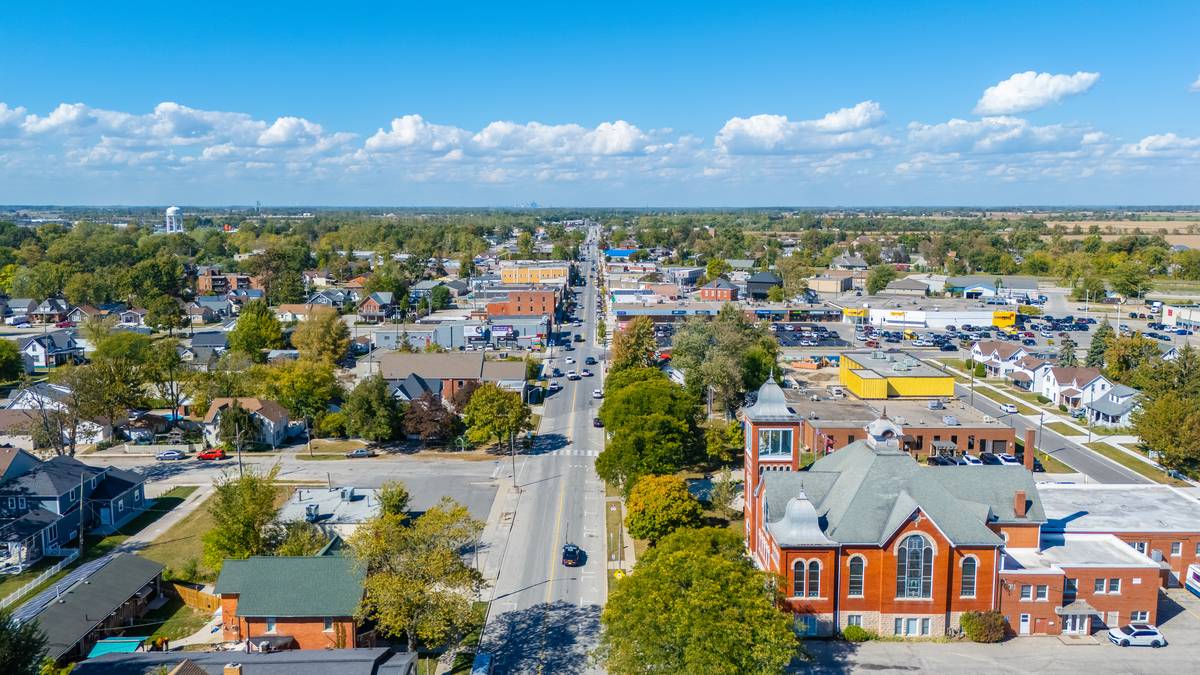 Aerial view over downtown Essex: shops lining the main street, a red-brick church in the foreground, homes on both sides, and county farmland along the horizon.
