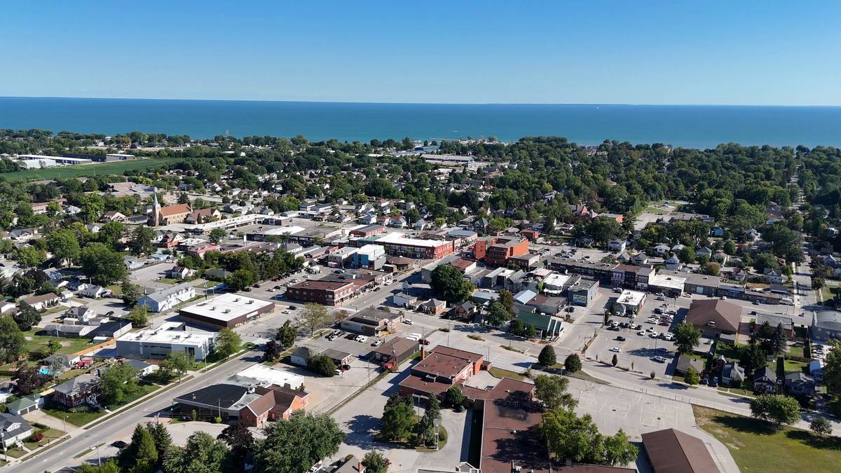 Aerial view over Kingsville: shops and brick storefronts along Main Street, a church spire and homes among mature trees, and Lake Erie along the horizon.