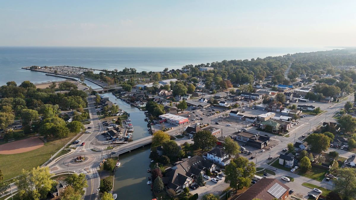 Aerial view over Belle River in Lakeshore: the river running past the town centre to the marina, homes and shops on both banks, and Lake St. Clair along the horizon.