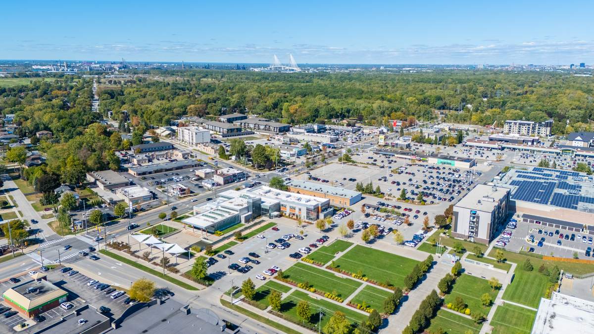 Aerial view over LaSalle's civic centre: landscaped lawns and public buildings, surrounding low-rise development and neighbourhoods, with the Detroit skyline on the far horizon.