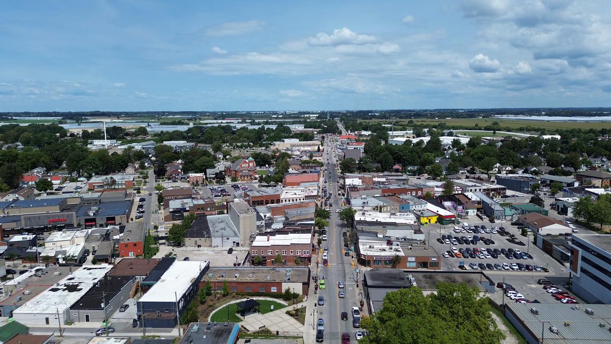 Aerial view over uptown Leamington: shops and storefronts lining Talbot Street, homes on the streets behind, and the greenhouse landscape along the horizon.