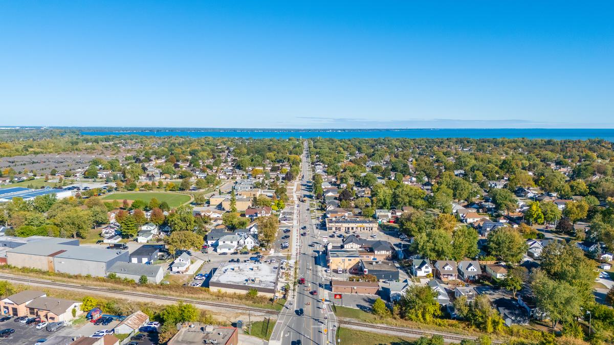 Aerial view north over Tecumseh: a main road running between residential streets and low commercial blocks, with Lake St. Clair filling the horizon.