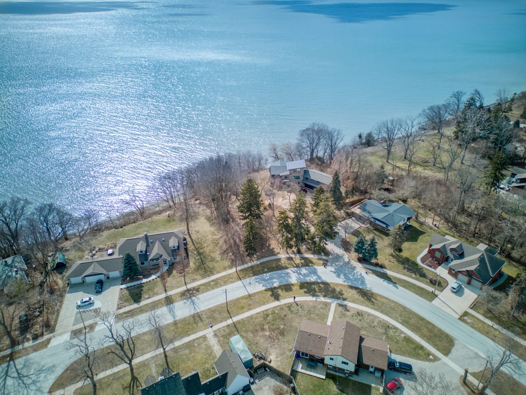 Aerial view over Briarwood Crescent in Kingsville toward Lake Erie, with wooded lakefront lots between the homes and the water