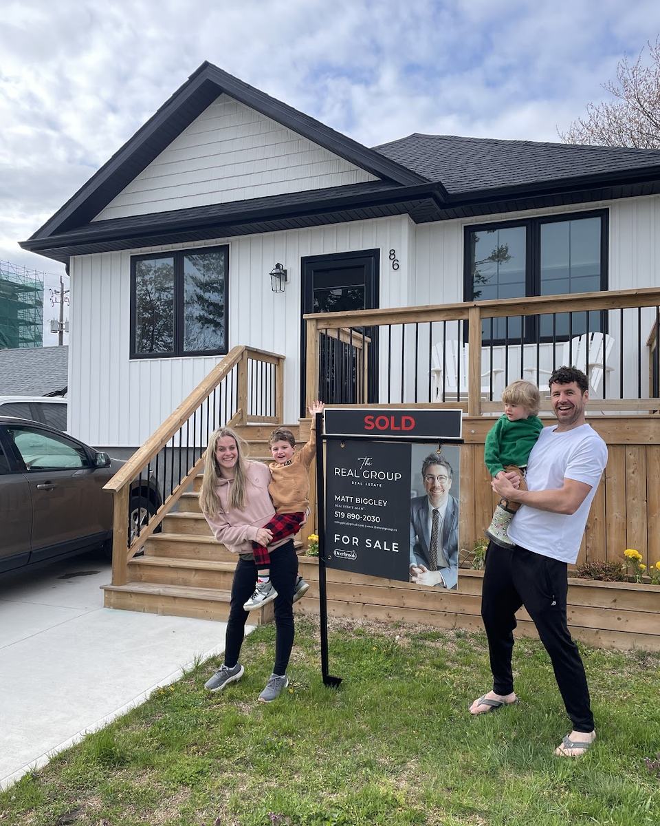 A family with two young children beside a Sold sign on the front lawn of the home Matt Biggley sold for them